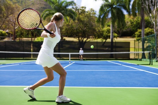 Two people playing tennis in a tropical setting